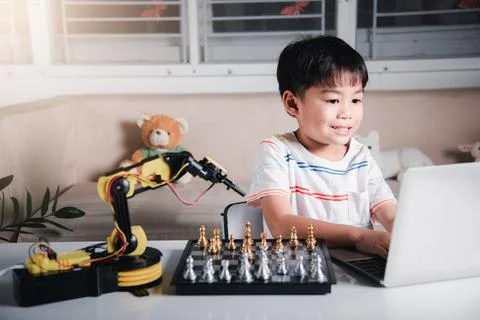 Asian little boy programming code to robot machine arm on laptop for play che Foto stock