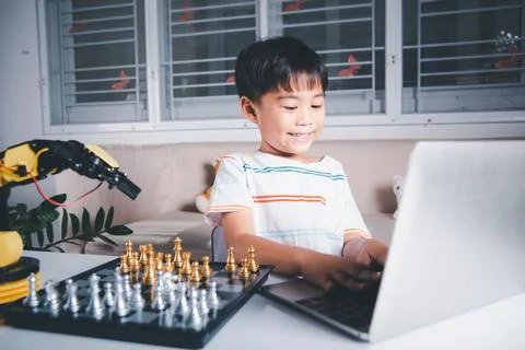 Asian little boy programming code to robot machine arm on laptop for play chess Foto stock