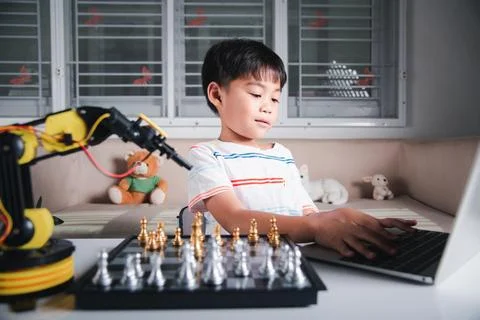 Asian little boy programming code to robot machine arm on laptop for play chess Foto stock
