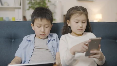 Asian little kids busy with gadgets, playing online games, technology addiction Stock Footage