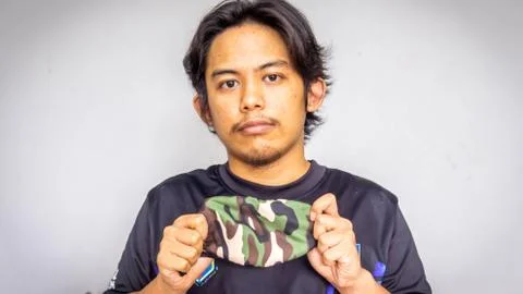 Asian Malay man holding army camouflage face mask on isolated white background. Stock Photos