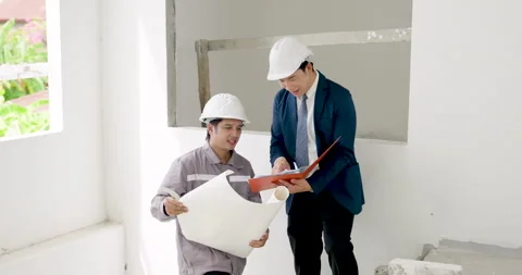 Asian male engineer and contractor review blueprint together inside unfinished Stock Footage 336534741