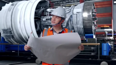 Asian Male Engineer Looking At Blueprint In His Hands With Jet Engine Stock Footage 306599490