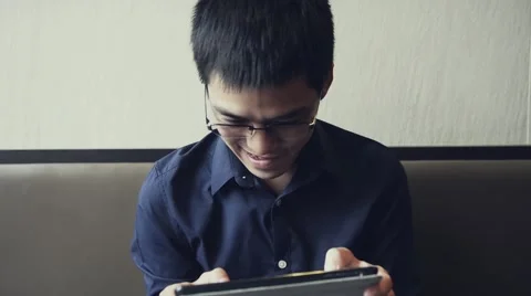 Asian male enjoy using tablet to play game Stock Footage 63398548