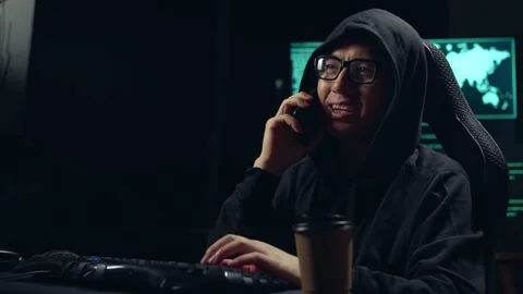 Asian Male Hacker Using Computer Hacking And Calling Phone Stock Footage 157327532