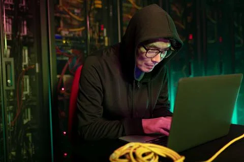 Asian male hacker using a laptop in computer server room Stock Photos