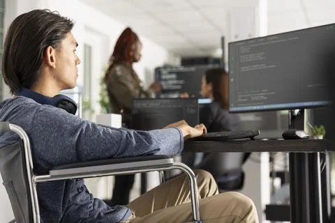 Asian male programmer coding in wheelchair at office Stockfoto's