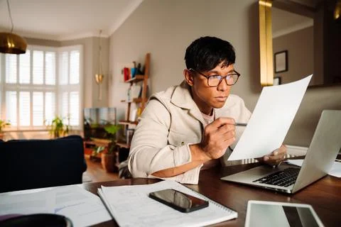 Asian male reading document while working from home Stock Photos