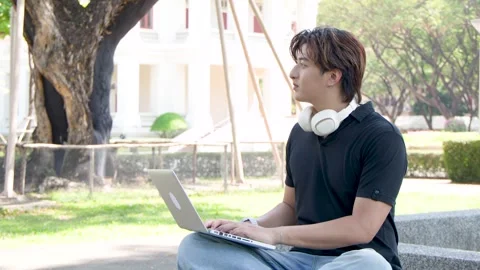 Asian Male Student Using Laptop Outdoors on University Campus Grounds Stock Footage 336352183