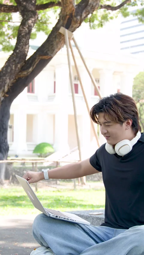 Asian Male Student Using Laptop Outdoors on University Campus Grounds Stock Footage 337600438