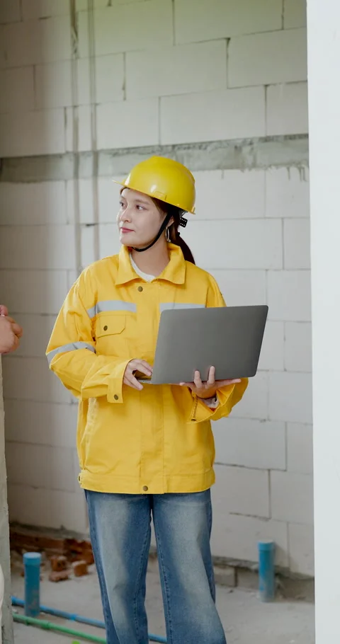 Asian male supervisor explains wall issue to woman engineer holding laptop, Stock Footage 339841807