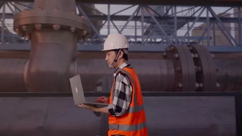 Asian Male Use Computer While Walking with Industrial Pipeline Stock Footage 318079337