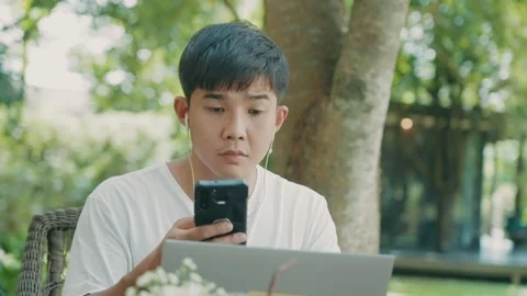 Asian male using cellphone doing online task with laptop computer Stock Footage 270320143