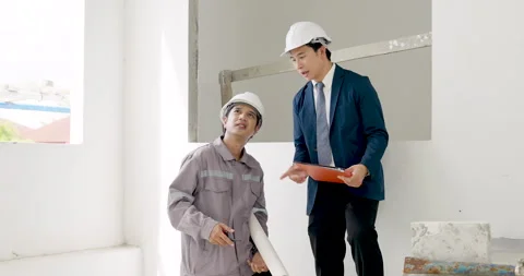 Asian male worker points upward while engineer holds project folder, discussing Stock Footage 345222982