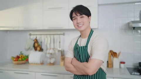 Asian man in apron smiling to camera while standing with arms crossed in kitchen Video stock 241773846
