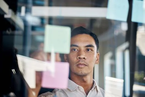 An Asian man brainstorms with sticky notes as seen through a window Stock Photos