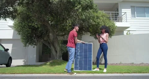 Asian man bringing solar panel, placing at curb for install while woman checking Stock Footage 341320256