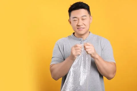 Asian man with bubble wrap on orange background. Space for text Stock Photos