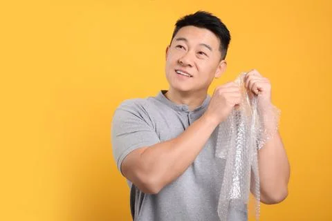 Asian man with bubble wrap on orange background. Space for text Stock Photos