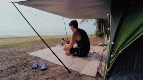 Asian man camping and play guitar on the beach Stock Footage 155116653