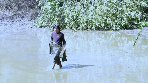 An Asian man casts a net to find fish in a dry pond. Stock Footage 259690864