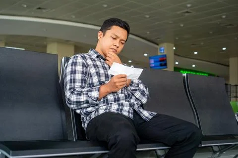 Asian man checking his plane ticket while using mobile phone in airport wai.. Stock Photos