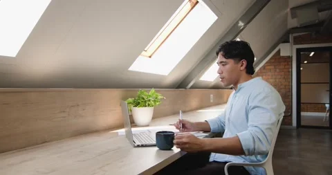 Asian man checking laptop for work, writing notebook and sipping coffee at loft Stock Footage 339959120