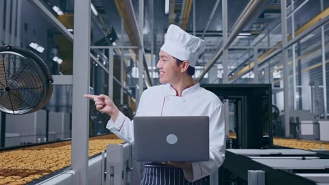 Asian Man Chef Using A Laptop And Pointing To Side In Cookie Factory Vidéo 318080765
