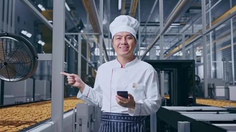 Asian Man Chef Using Smartphone And Pointing To Side In Cookie Factory Vidéo 318080583