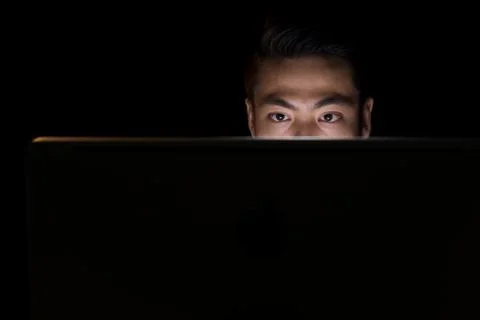 Asian man in darkness using compute Stock-Fotos