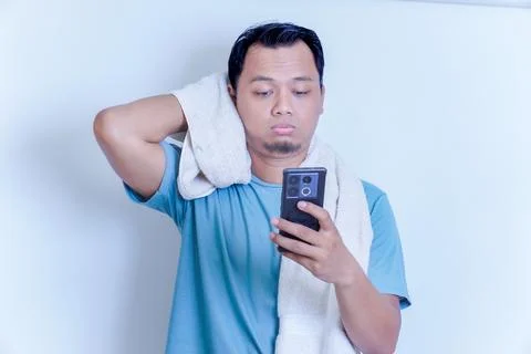 An Asian man with a disappointed expression while holding his smartphone an.. Stock Photos
