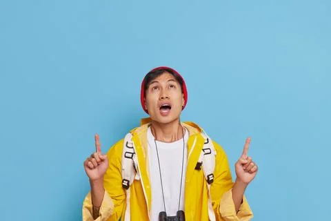 Asian man dressed in yellow jacket coat and red hat looks up and points fingers Stock Photos