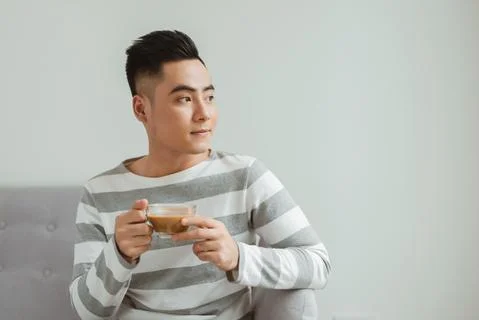 Asian man drinking coffee when sitting on sofa at home. Stock Photos