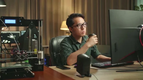 Asian Man Drinking Coffee While Works On Personal Computer And 3D Printer Stock Footage 158107621