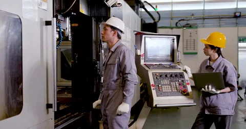 Asian man engineer checks CNC machine area as Asian woman technician reviews Stock Footage 338072657