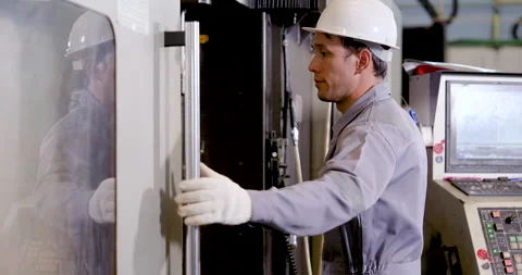 Asian man engineer closes CNC machine door after workspace review, completing Stock Footage 341398531