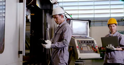 Asian man engineer examines CNC machine area while Asian woman technician reads Stock Footage 337285122