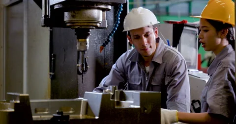 Asian man engineer leans toward CNC fixture while Asian woman technician Stock Footage 338071076
