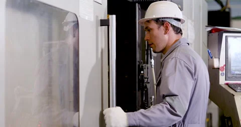 Asian man engineer slides CNC machine door while reviewing internal workspace, Stock Footage 338074192