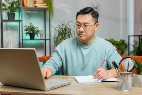 Asian man freelancer making notes on notebook at home, use laptop, prepare 库存照片