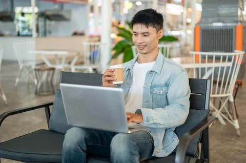 Asian man freelancer using laptop and holding coffee cup in cafe, represent.. 写真素材