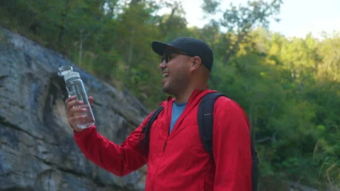 Asian man hiker  taking a break to drink from a rock within the national park. Видео 342409818
