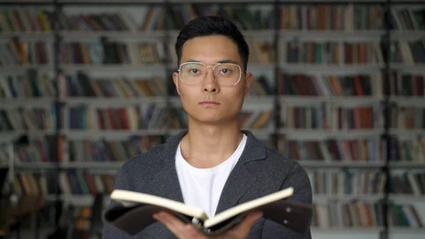 Asian man holding a blocknote standing looking straight ahead in the library 스톡 동영상 110852975