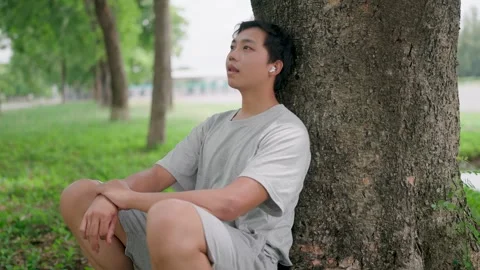 Asian man leaning on a tree thinking outside sitting on floor, Video stock 283187189