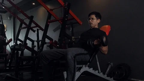Asian man lifting weights seated dumbbell  bicep curl in gym training. Stock Footage 106290688