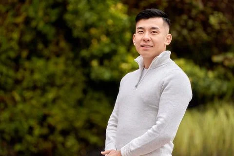 Asian man looking at the camera while relaxing outdoors in a park. 写真素材