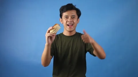 Asian man looking hungry holding hamburger while giving thumbs up Stock Footage 323779494