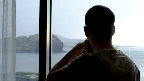 Asian man looking out window and drinking coffee back view, concept of vacation Stock Footage 233304844