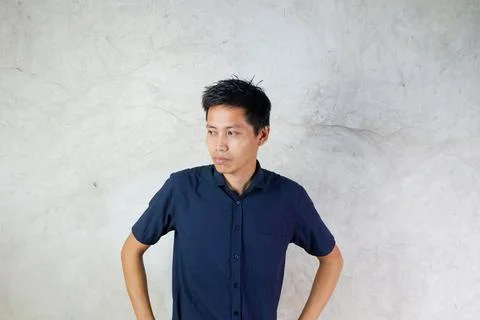 Asian man looking sideways down hands on waist. wall background Stock Photos