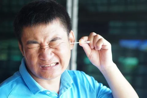 Asian man make face expression during using cotton bud stick to remove earwax. C Stock Photos